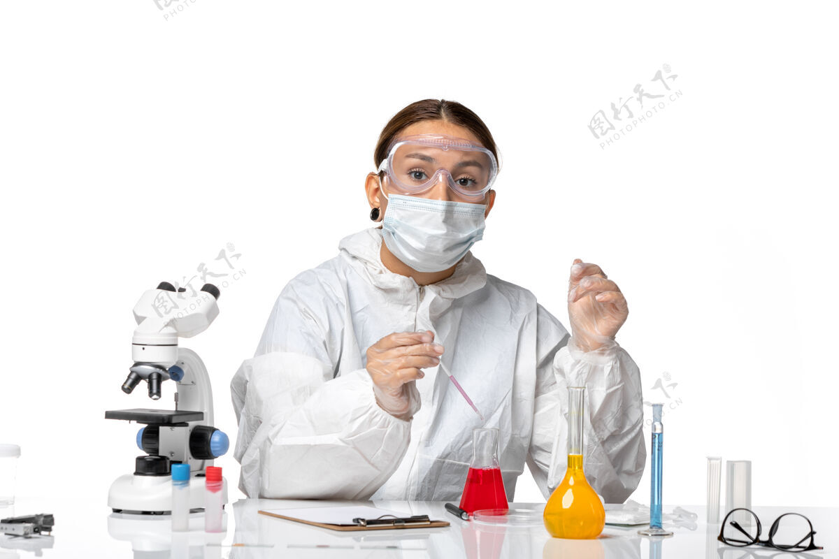 实验室外套前视图穿着防护服 戴着面罩的女医生正在用浅白色背景的冠状病毒大流行病毒冠状病毒溶液工作视图实验室医院