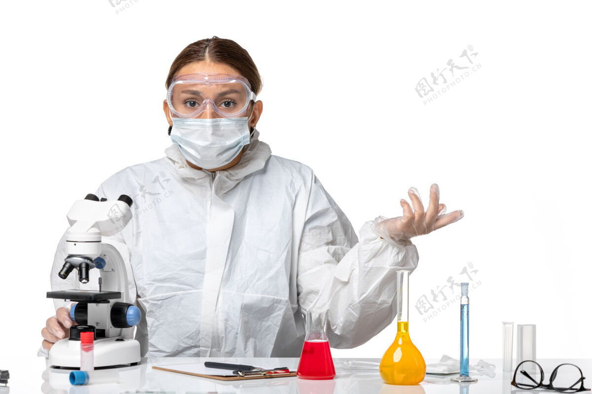 病毒前视图女医生穿着防护服 戴着口罩 用显微镜观察浅白色背景的医学病毒-健康大流行病毒套装实验室外套大流行