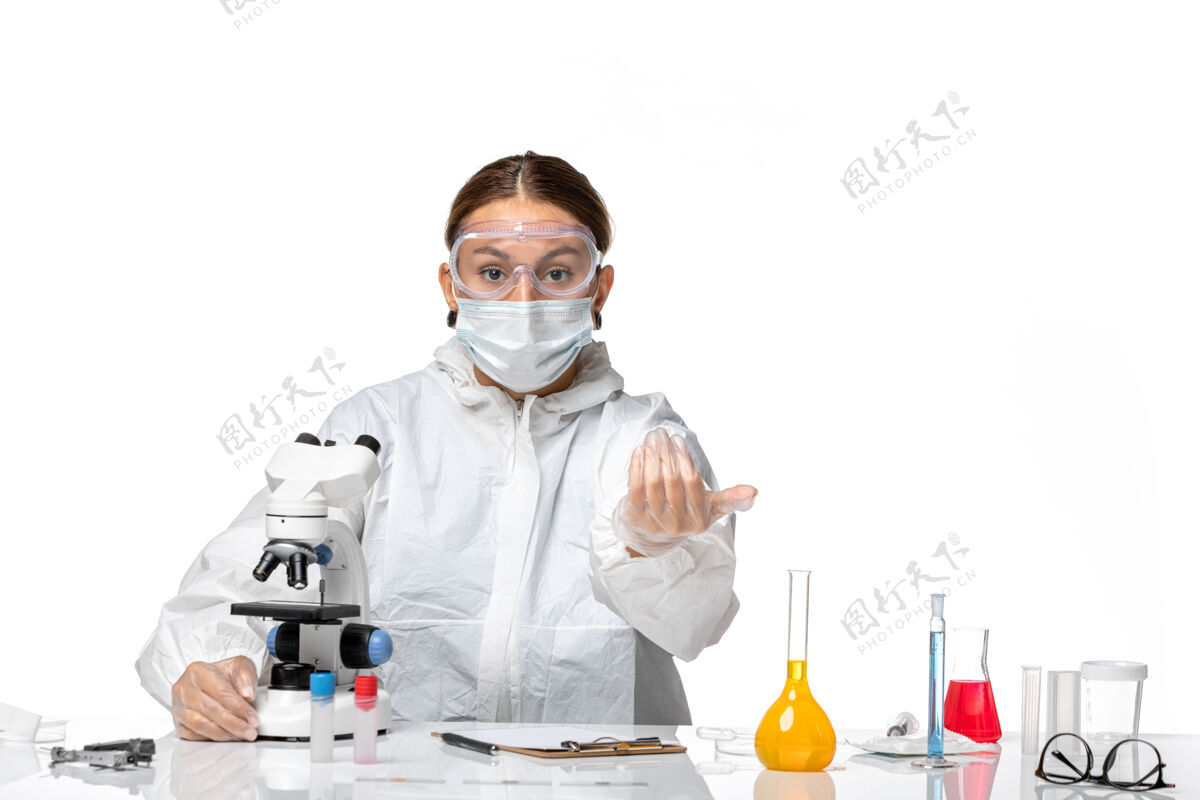 医疗前视女医生穿着特制的西装 戴着口罩 用显微镜和白色办公桌上的人打电话冠状病毒大流行呼叫前台医生