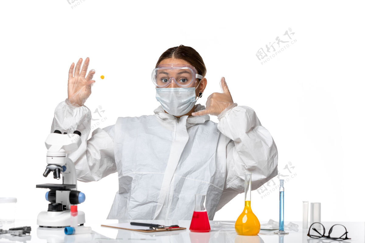 白色前视图：穿着防护服 戴着面罩的女医生 在浅白色背景上拿着样本 药物是柯维病毒-大流行病毒伪装大流行呼叫