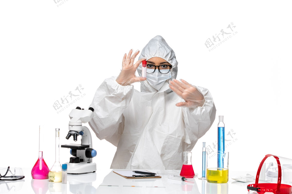 桌子正面图穿着特殊防护服的女化学家拿着白桌子上的空瓶子病毒健康化学病毒套装病毒视图