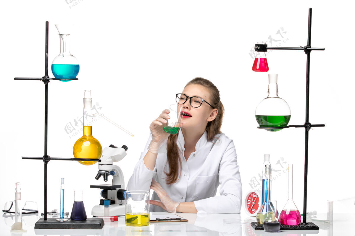 前排前视图穿着医疗服的女化学家坐在白色背景上 用不同的溶液化学大流行健康病毒健康专业套装
