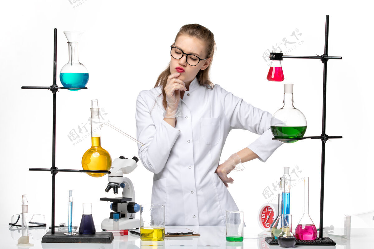 人前视图身着医疗服的女化学家站在白色背景上的不同溶液前化学大流行性冠状病毒思想实验室观点
