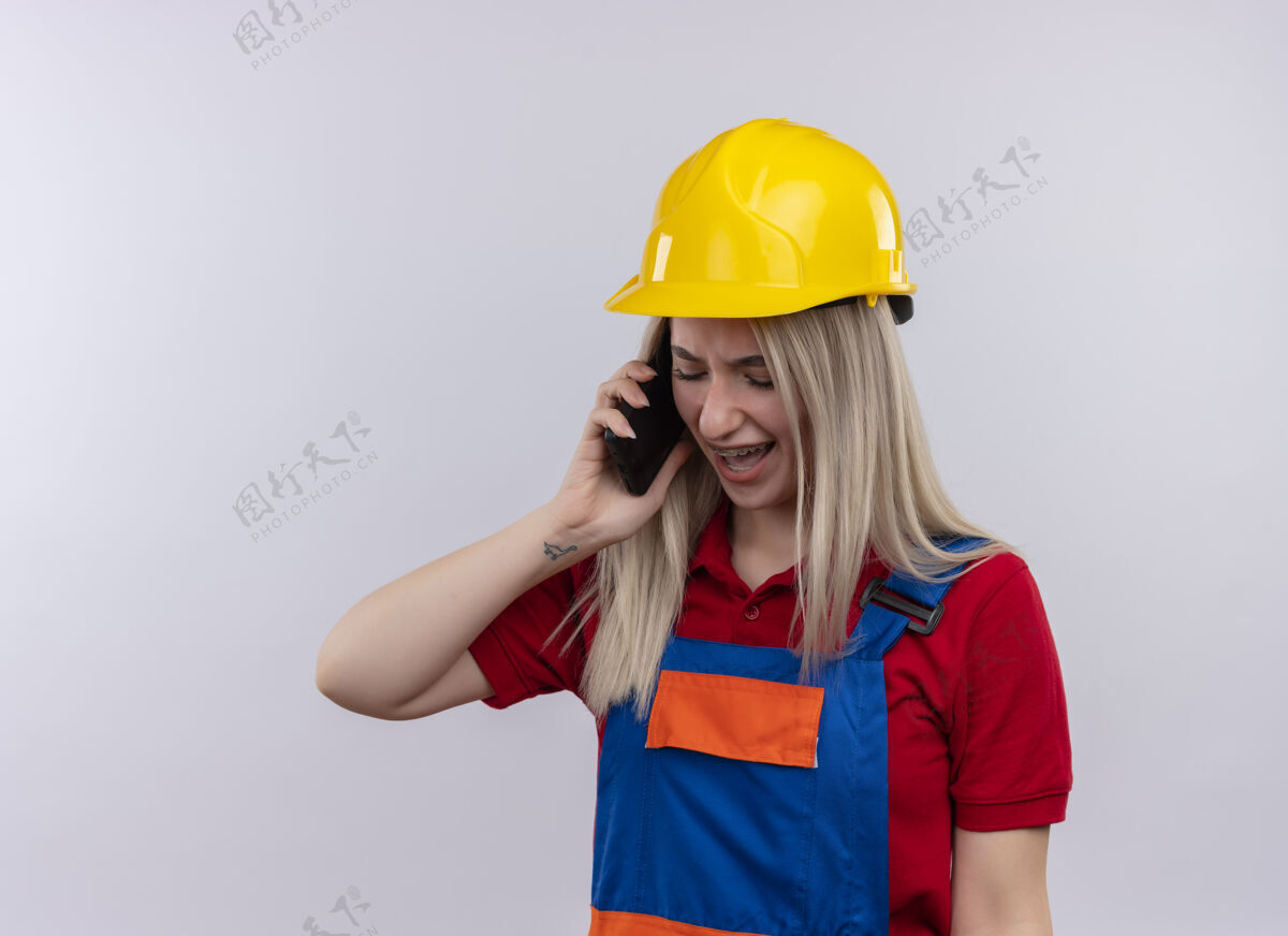 愤怒愤怒的年轻金发工程师 穿着制服 戴着牙套的建筑工女孩 在隔离的空白处和复印件区打电话牙科牙套制服