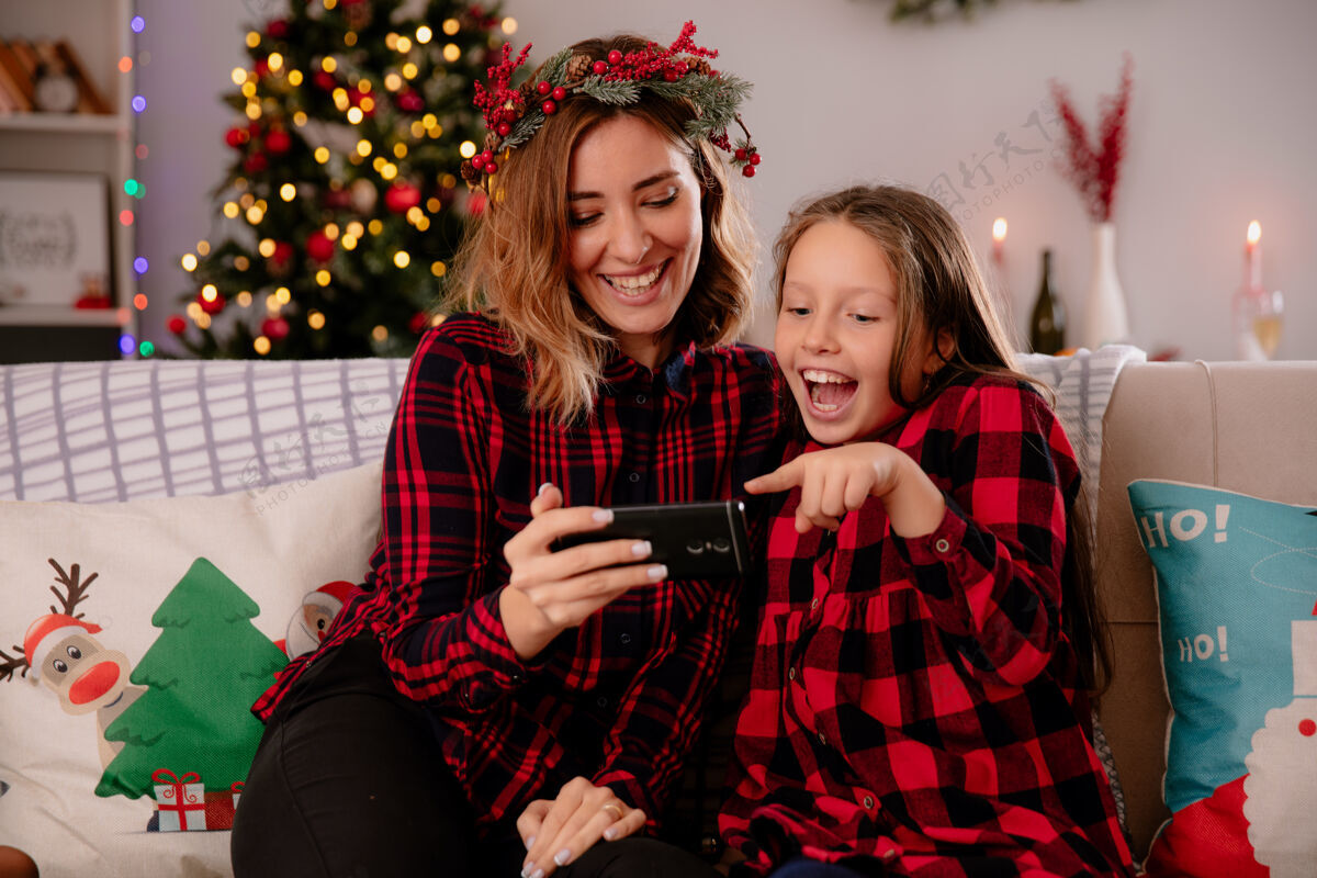 时间笑眯眯的母女俩坐在沙发上看电话 在家里享受圣诞节时光电话看女儿