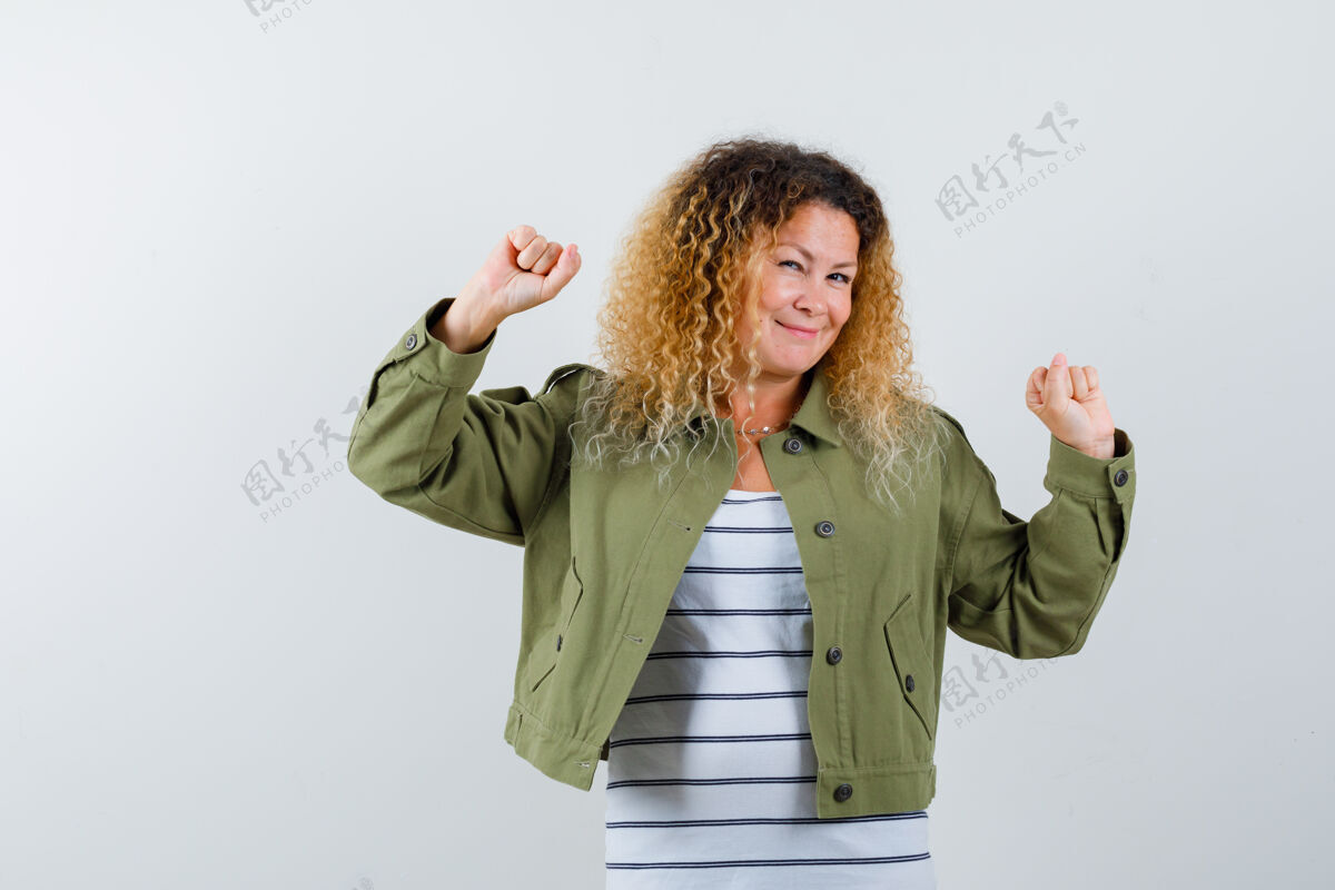 年轻一个金发卷曲的女人 穿着绿色夹克 摆出一副获胜者的姿态 看上去很快乐 正前方的风景女士漂亮肖像