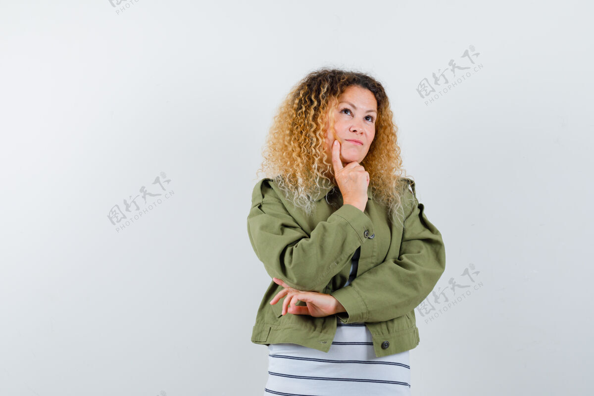 手一位金发卷曲的女士 手上托着下巴 穿着绿色夹克 看上去很体贴 正前方的景色夹克时尚专业