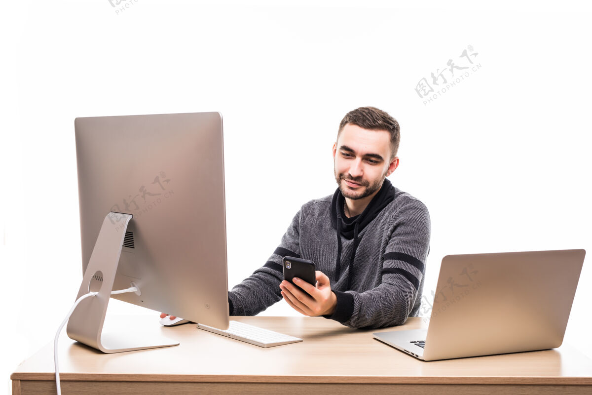 商务帅气的企业家坐在办公桌后面 拿着笔记本电脑和个人电脑 用白色的手机打字文案空间男士办公室