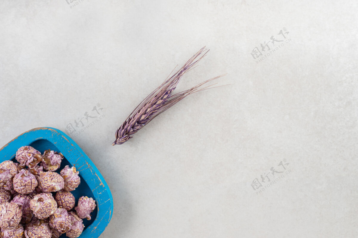 果仁紫色的麦秆放在大理石桌上一个蓝色的木盘旁 上面放着一盘普罗普尔爆米花小吃顶视图小麦