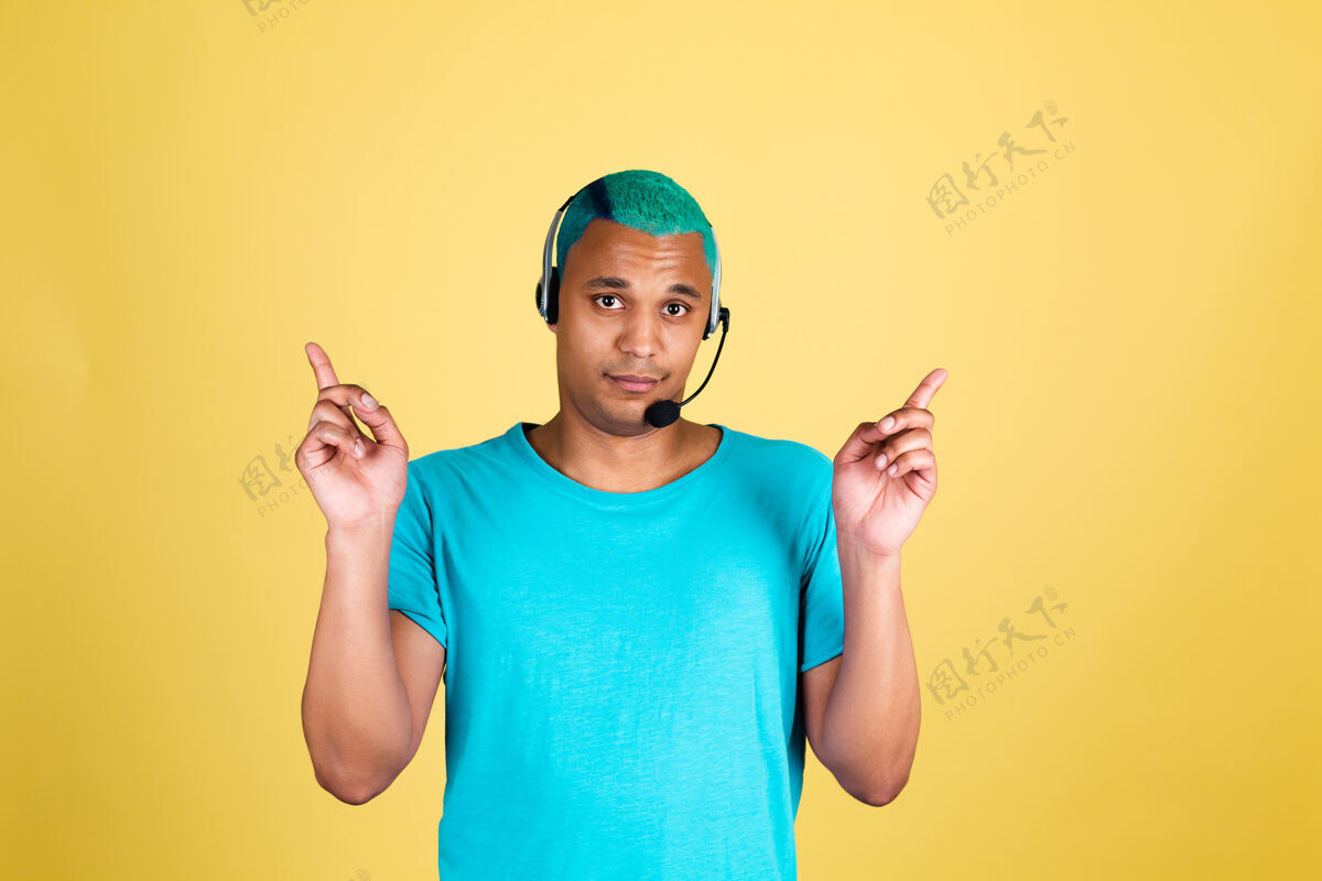 智能休闲黑人非洲男子在休闲黄墙上蓝色头发呼叫中心工作人员快乐的客户支持接线员戴着耳机手指向上服务专业男性