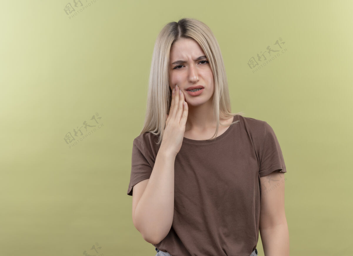 疼痛疼痛的年轻金发女孩把手放在脸颊上 忍受着牙痛 在隔离的绿色空间和复制空间牙痛痛苦绿色