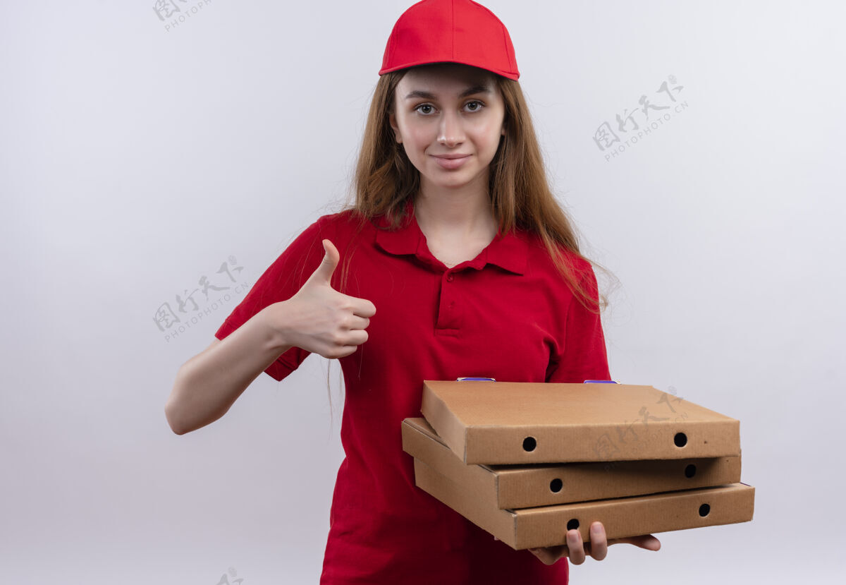 女孩穿着红色制服的自信的年轻送货女孩拿着包裹 在孤立的空白处竖起大拇指盒举行信心