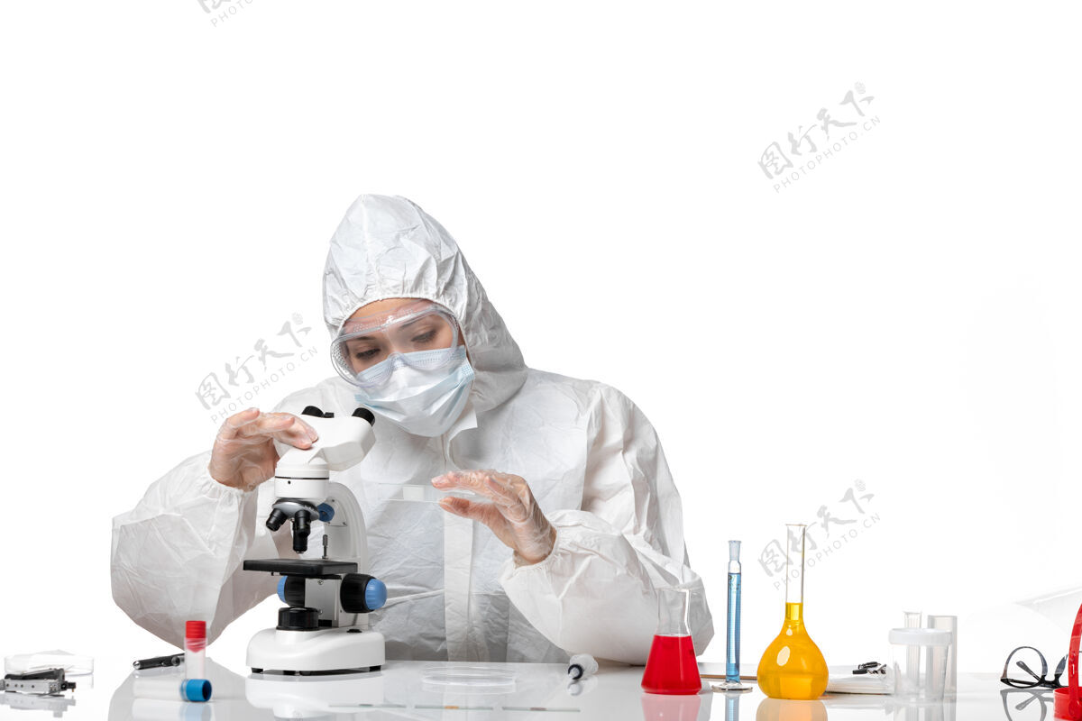 女医生前视图：女医生穿着防护服 戴着口罩 在显微镜下观察到病毒大流行时溅起的浅白色病毒正面面罩使用