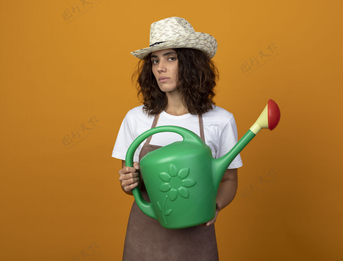 信心自信的年轻女园丁穿着制服戴着园艺帽拿着浇水罐年轻浇水帽子