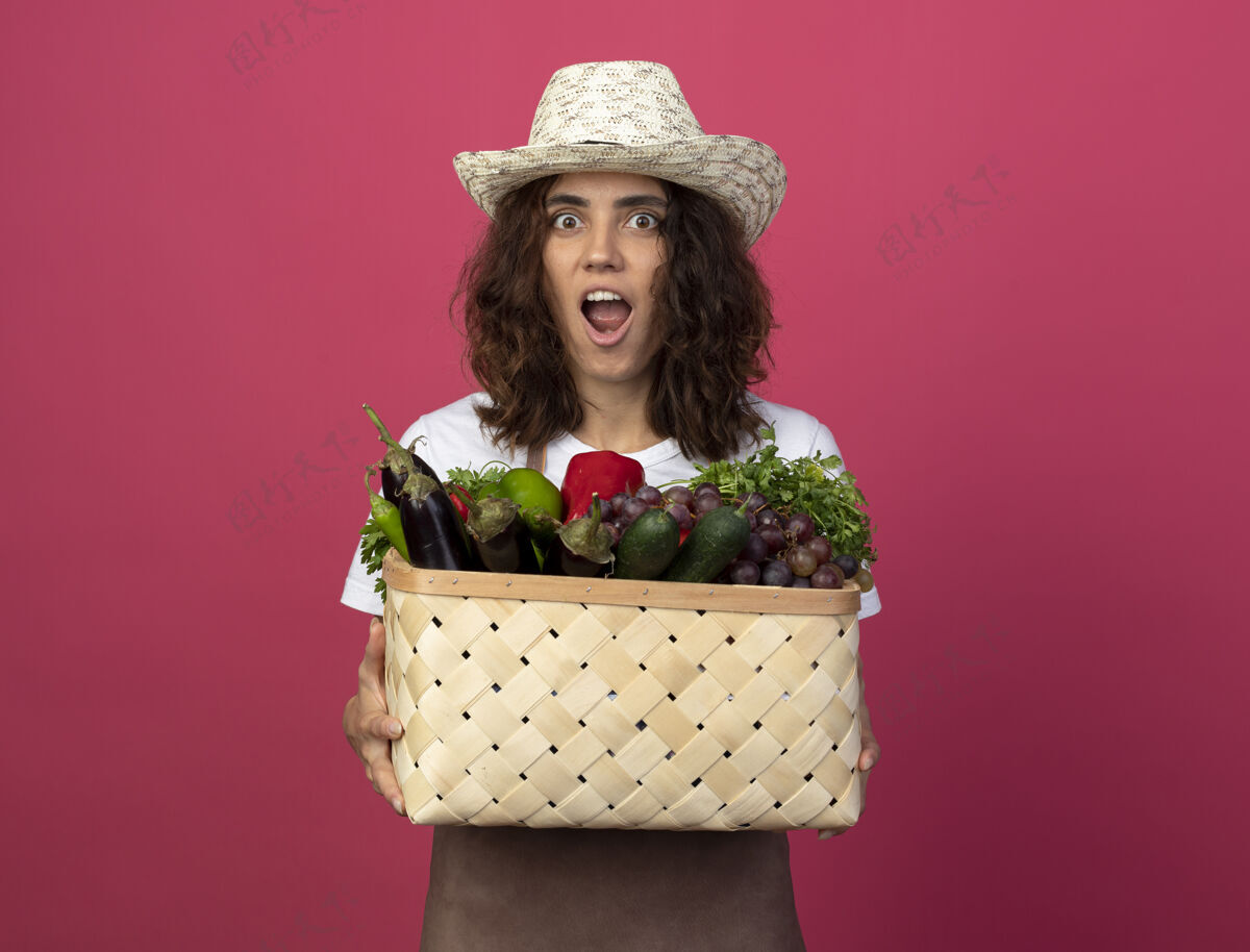 篮子穿着制服的年轻女园丁惊讶地戴着园艺帽 手里拿着菜篮子穿制服女人