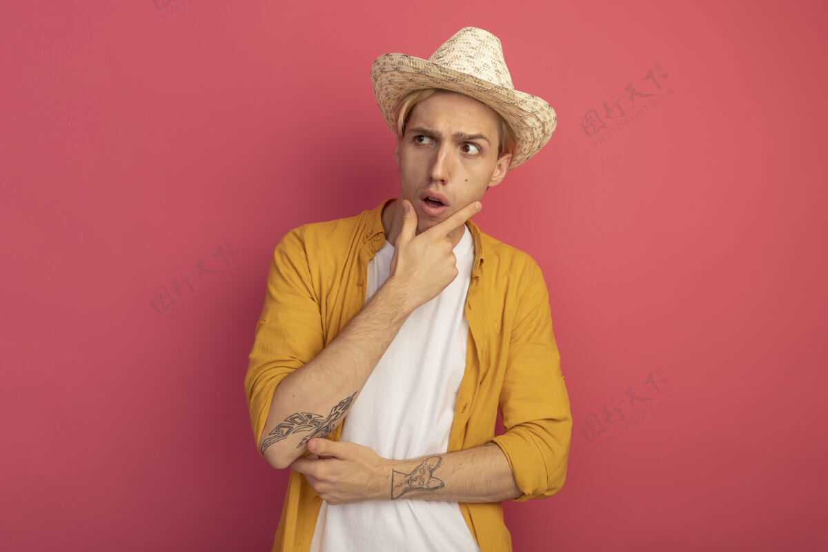 年轻困惑地看着身边年轻的金发男子穿着黄色t恤和帽子把手放在下巴下面手下巴帽子