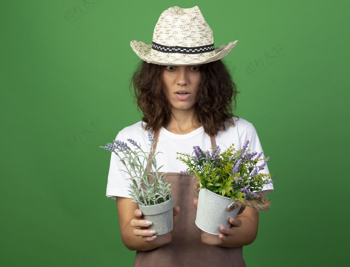 帽子穿着制服的年轻女园丁惊讶地戴着园艺帽 拿着花盆看花儿人制服女人