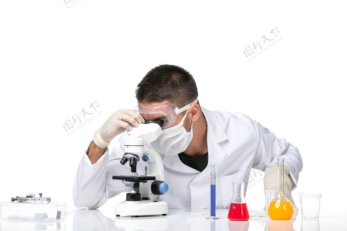 专业前视图：男医生穿着白色医疗服 戴着面罩 在白色空间使用显微镜显微镜使用健康
