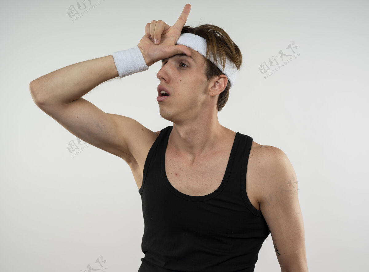 穿年轻的运动型男人一边戴着头带 一边戴着腕带 一边看着白色墙壁上的失败者姿态男人显示姿态