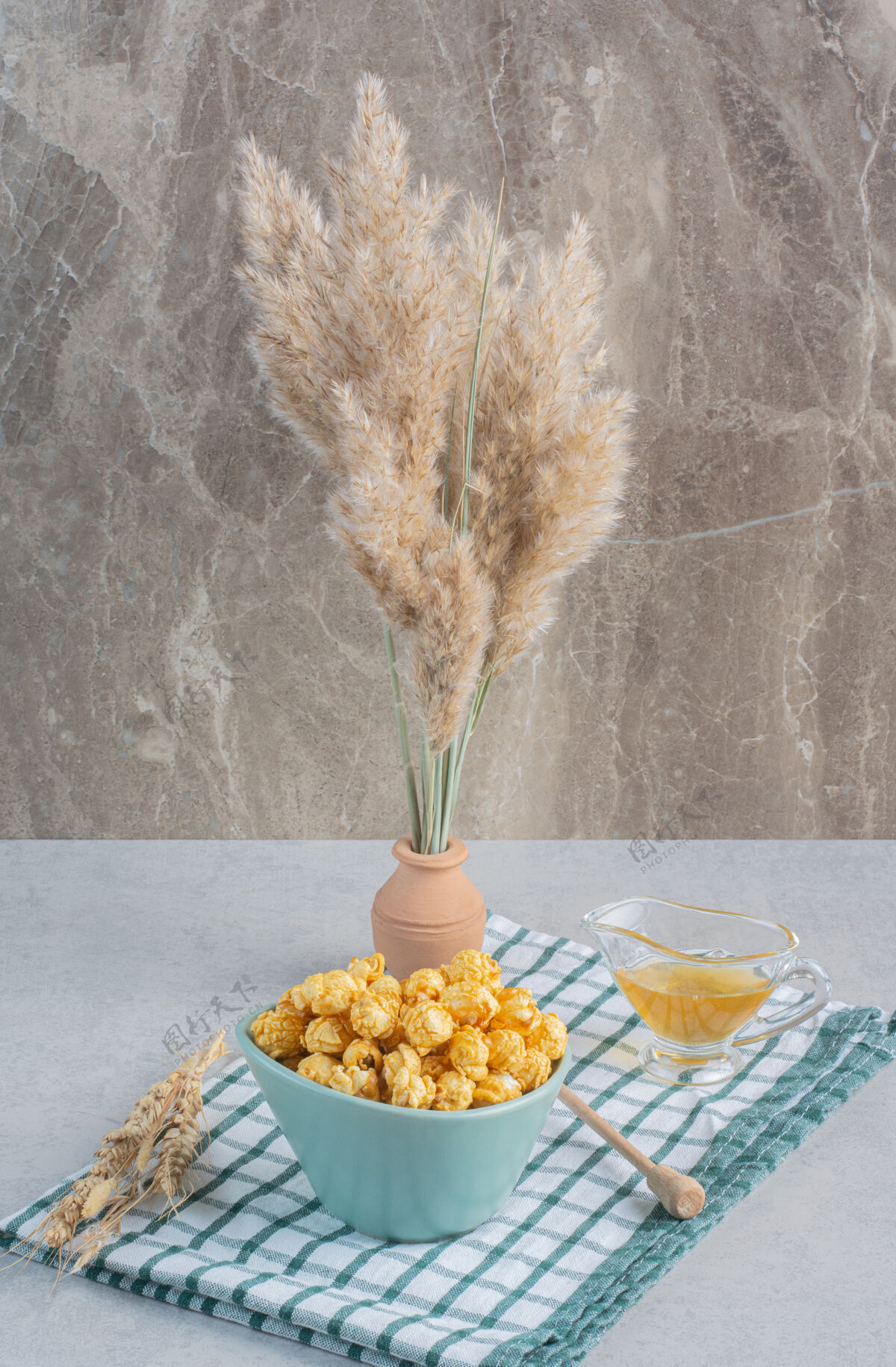 谷物一碗焦糖爆米花 一杯蜂蜜 一把蜂蜜勺和麦秆放在陶瓷花瓶里 放在大理石表面的毛巾上蜂蜜勺蜂蜜玻璃杯