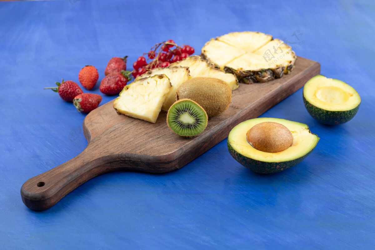 板一块木头砧板在蓝色的表面上切菠萝和奇异果红醋栗美味食品