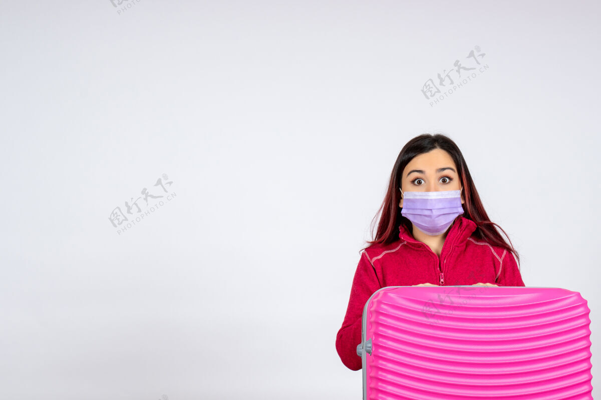 风景正面图年轻女性带着粉色的袋子在白墙上戴着口罩度假大流行病毒女性covid-彩色旅行颜色年轻女性病毒