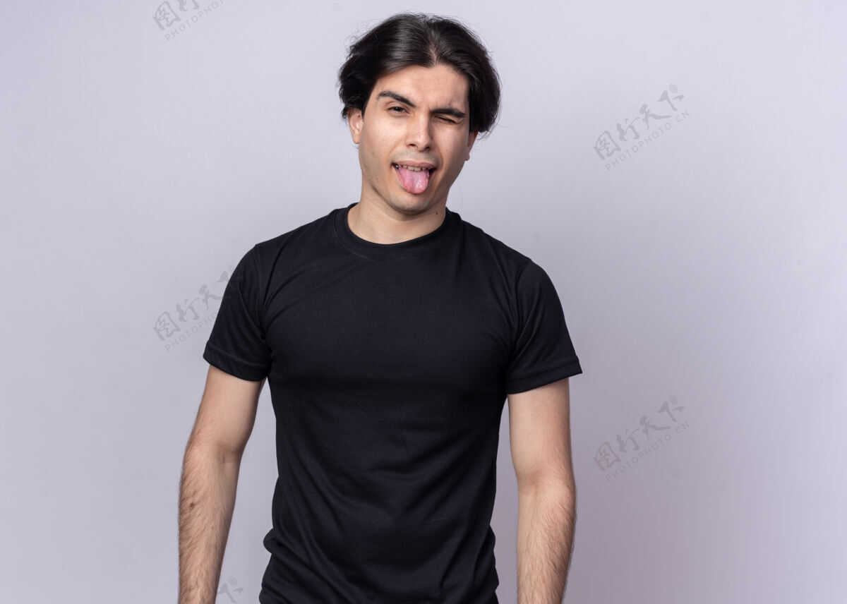 穿快乐的年轻帅哥穿着黑色t恤在白墙上露出孤立的舌头秀快乐帅气