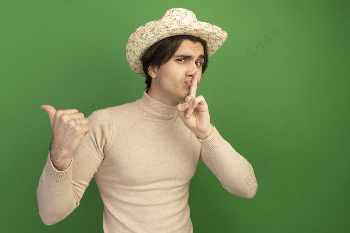 年轻年轻帅哥戴着帽子 沉默着 竖起大拇指 孤零零地站在绿色的墙上穿拇指严格