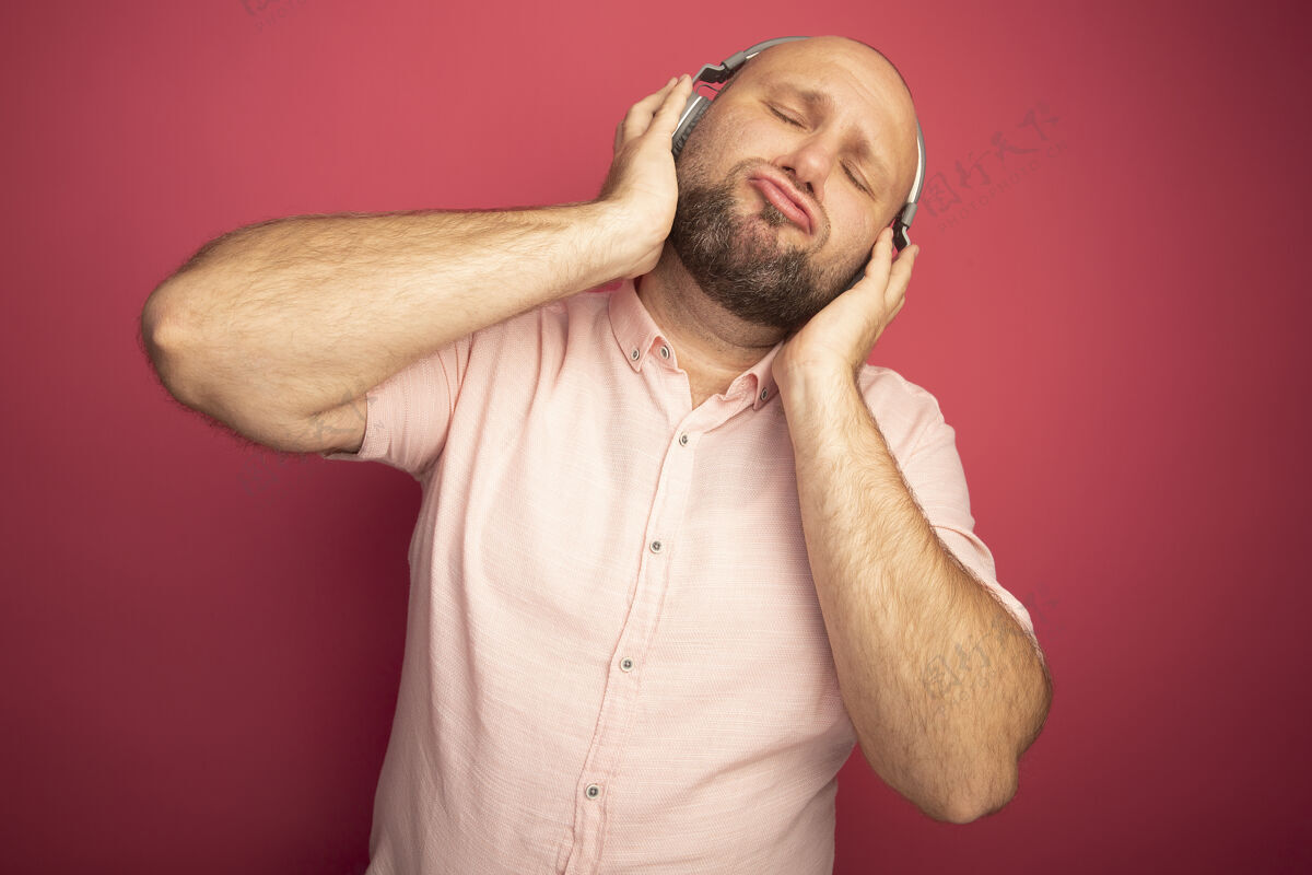 眼睛喜欢闭着眼睛的中年秃头男人穿着粉色t恤 戴着粉色隔离耳机耳机男人秃头