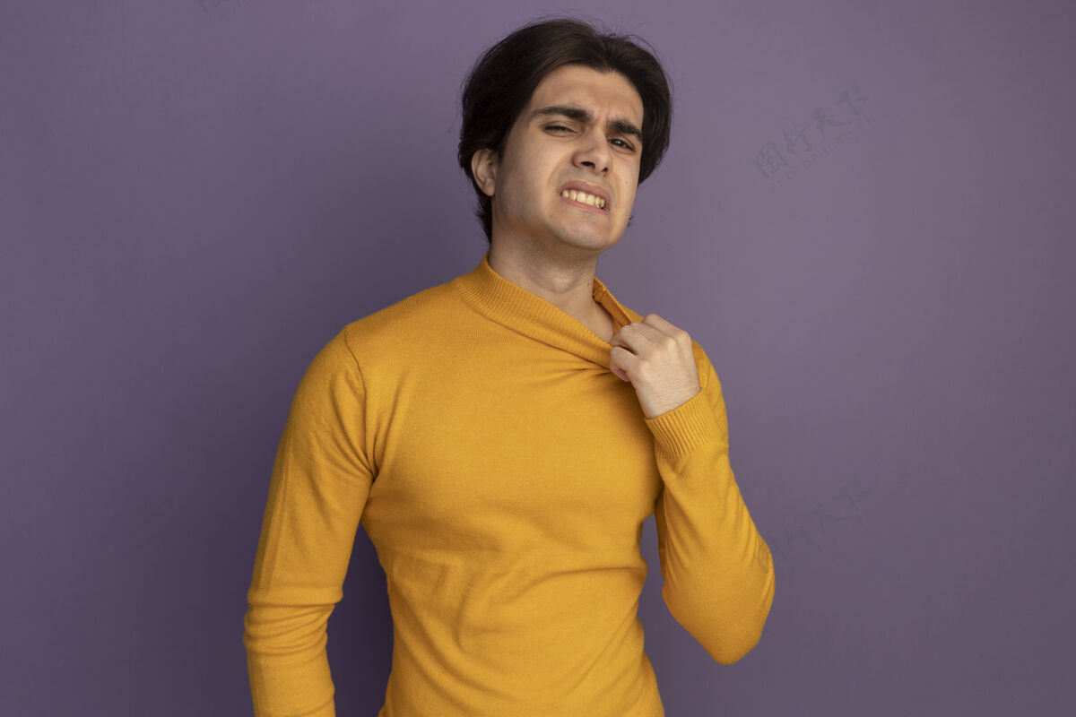 帅气穿着黄色高领毛衣的年轻帅哥拿着紫色的衣领孤立地站在墙上热高领毛衣抱着