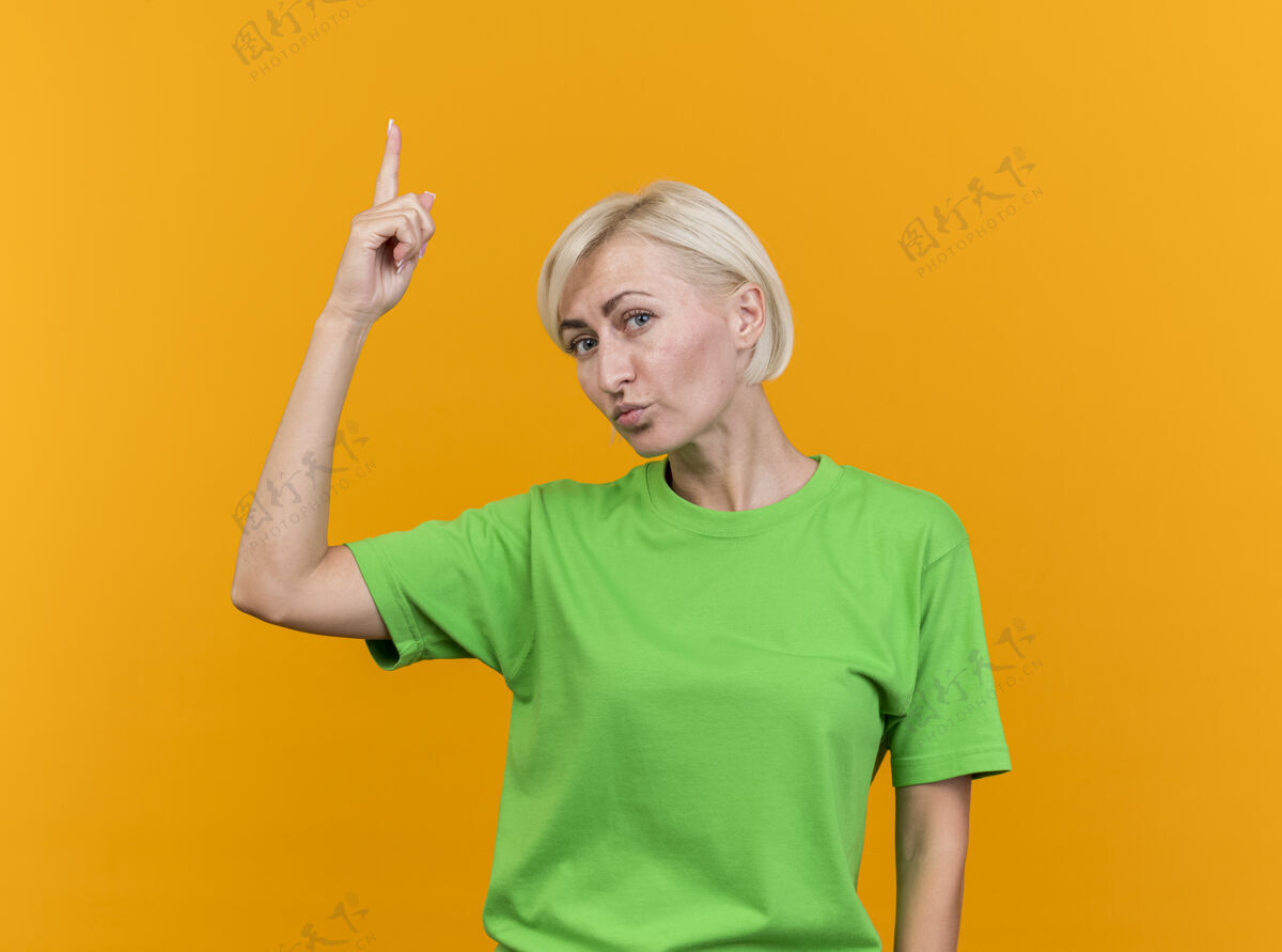 感觉自信的中年金发斯拉夫妇女看着前面指着隔离在黄色墙上的复制空间女人自信衣服