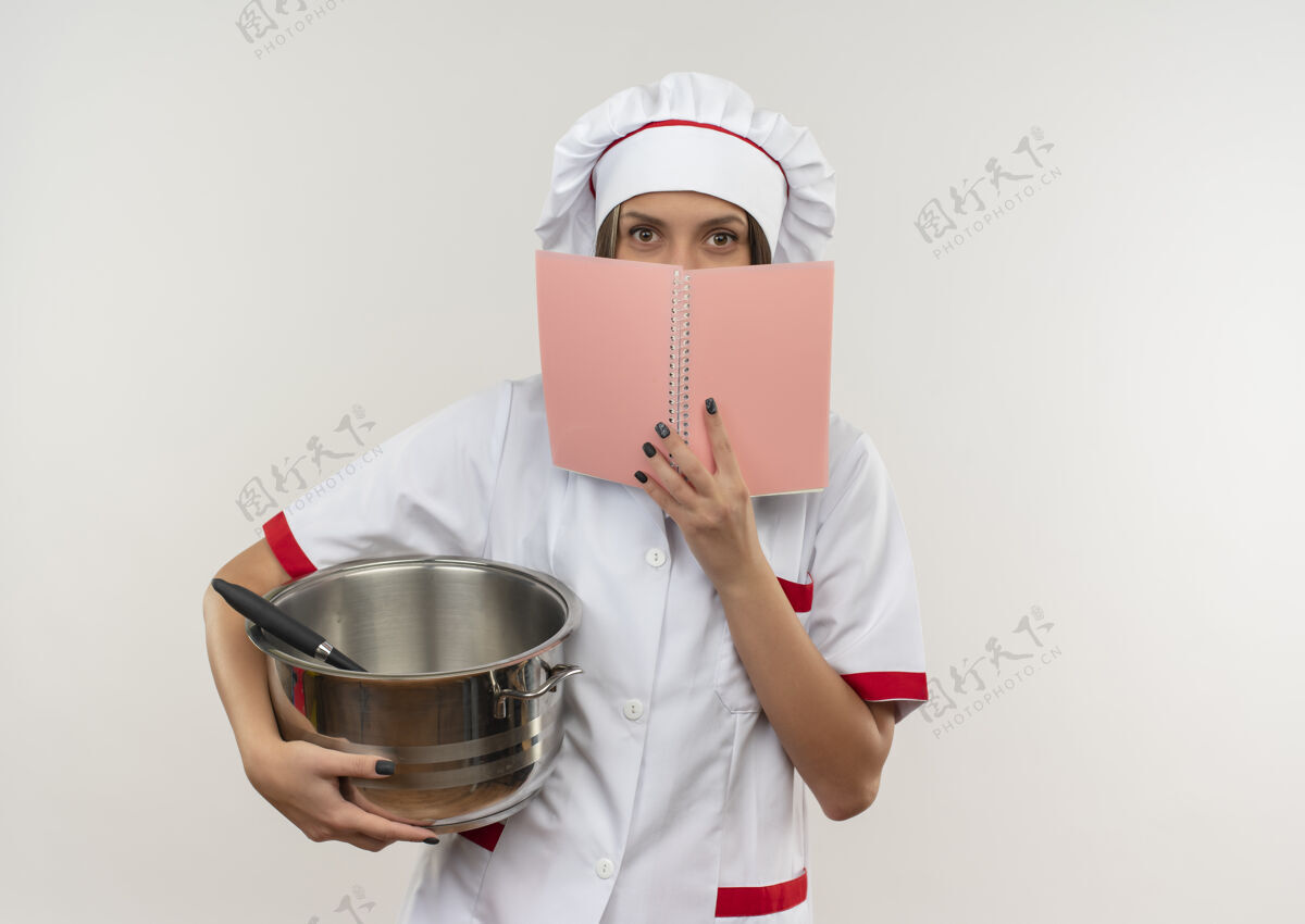 厨师穿着厨师制服的年轻女厨师拿着锅和便笺簿 从便笺簿后面看着相机 背景是白色的 有复印空间垫女相机