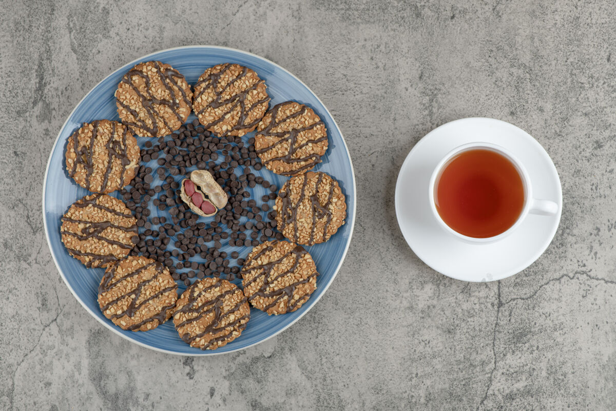 燕麦片蓝色盘子里放着巧克力饼干和一杯放在大理石上的花草茶零食内核美味