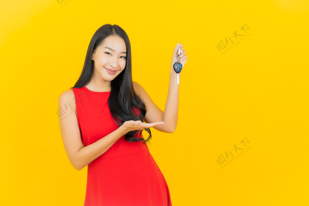 人画像美丽的亚洲年轻女子微笑着把车钥匙放在黄色的墙上女性女孩展示
