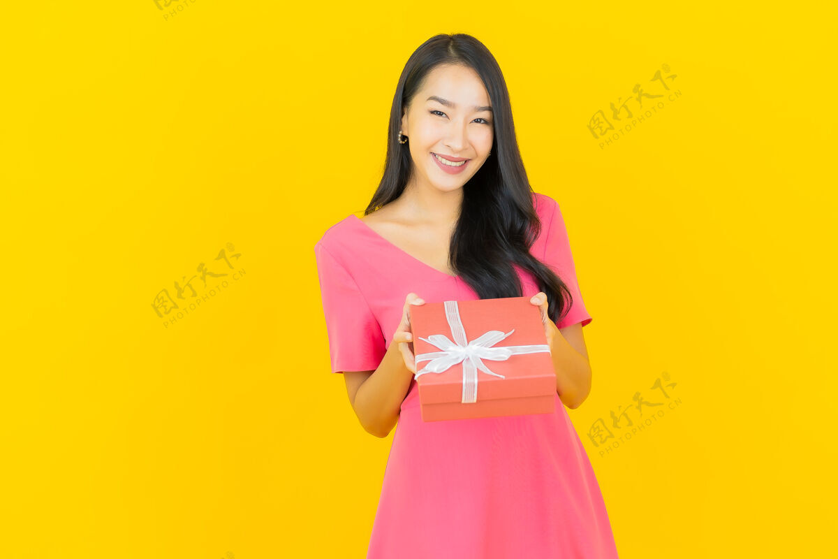 美丽肖像美丽的亚洲年轻女子微笑着黄色墙上的红色礼盒亚洲冬天微笑