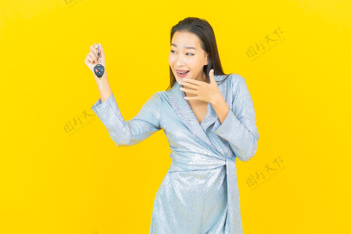 商业画像美丽的亚洲年轻女子微笑着把车钥匙放在黄色的墙上女人女孩黑人