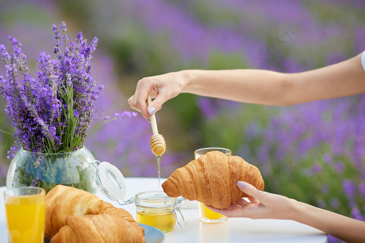 农作物在薰衣草地里 女人的手把蜂蜜放在羊角面包上花瓶蜂蜜匙美味