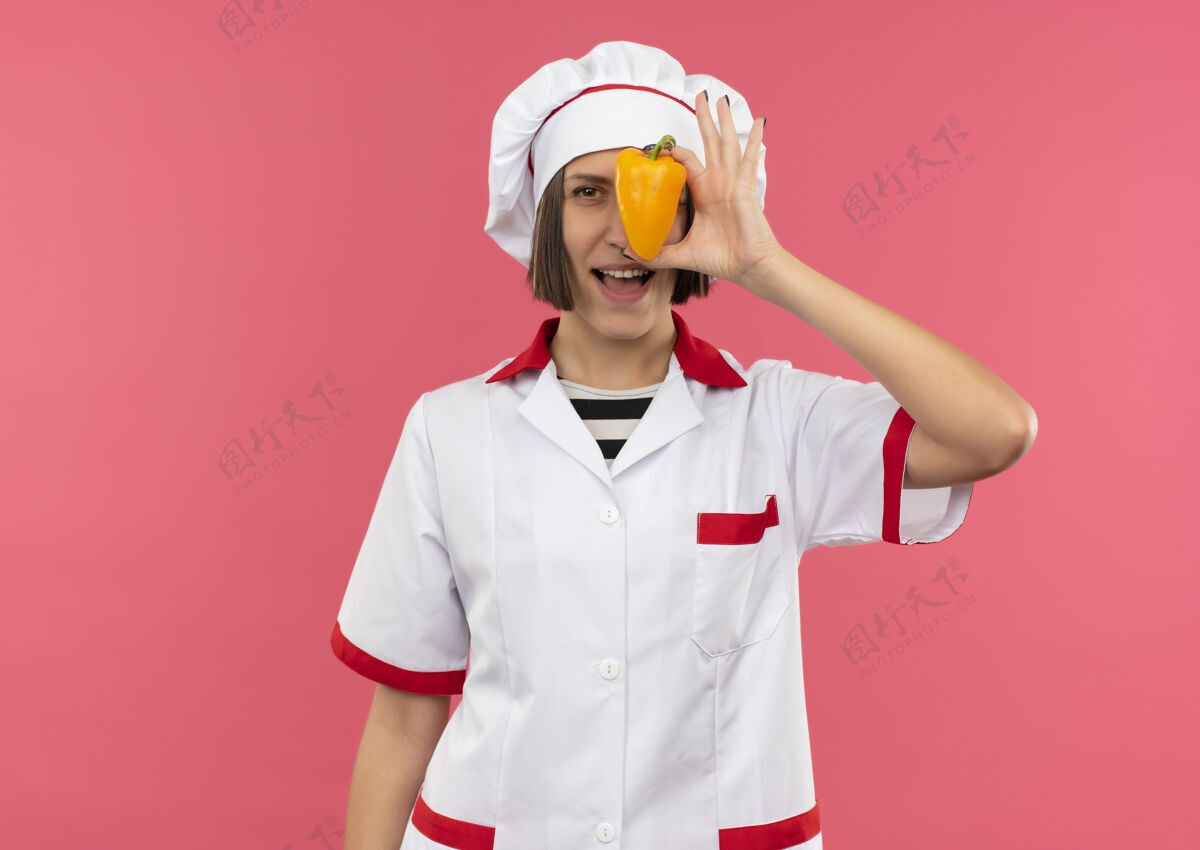 烹饪快乐的年轻女厨师身着厨师制服 从后面看着前面的粉红色辣椒隔离年轻制服粉红