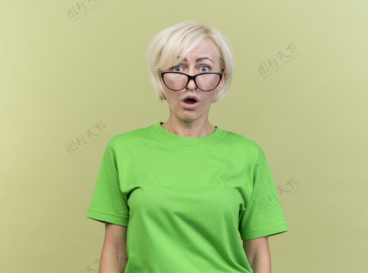 金发惊讶的中年金发斯拉夫女人戴着眼镜 看着前面孤立的橄榄绿墙上有复印空间人斯拉夫市民
