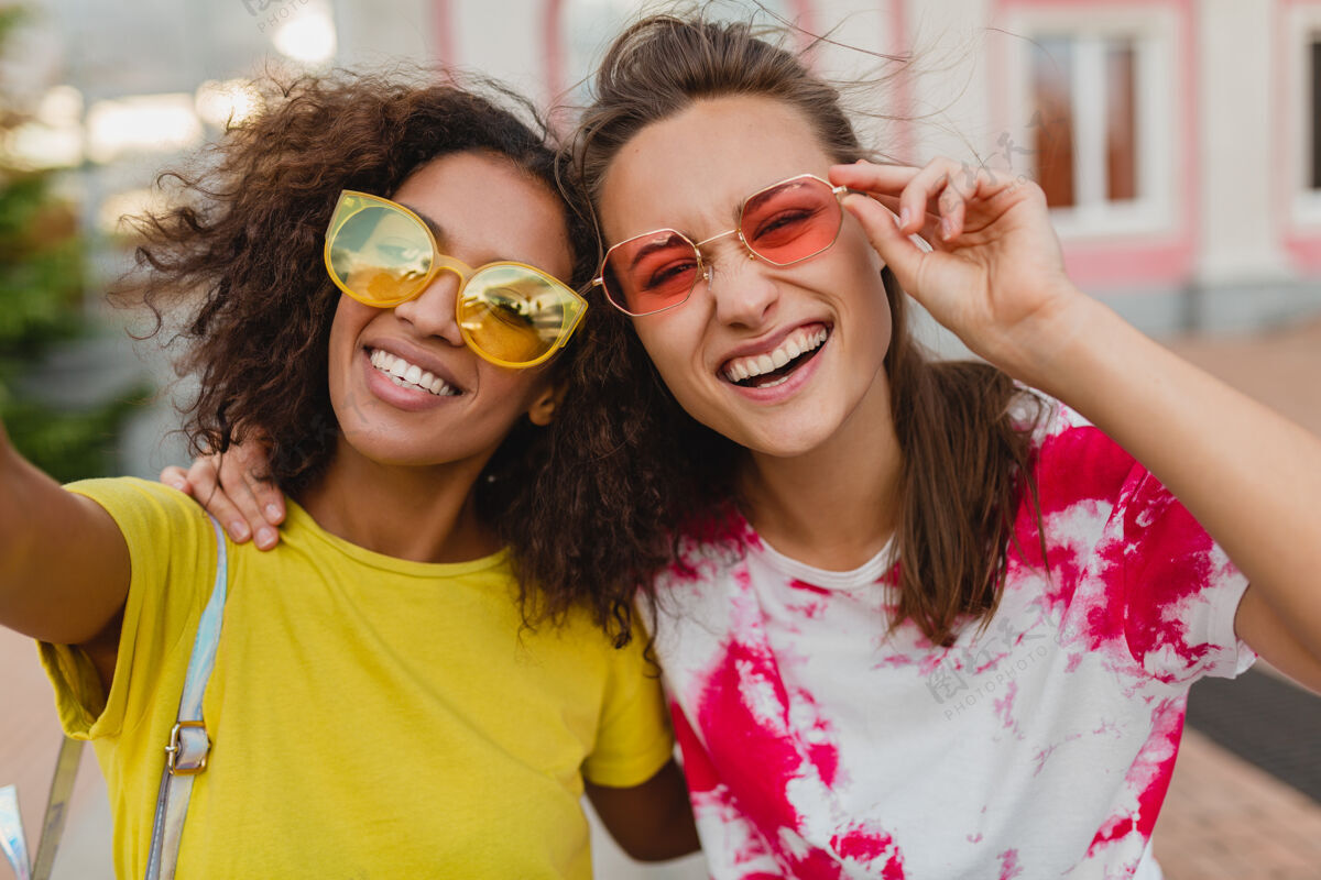 多民族五颜六色的照片 快乐的年轻女孩朋友们微笑着坐在街上用手机自拍 女人们在一起玩得很开心非洲裔太阳镜眼镜