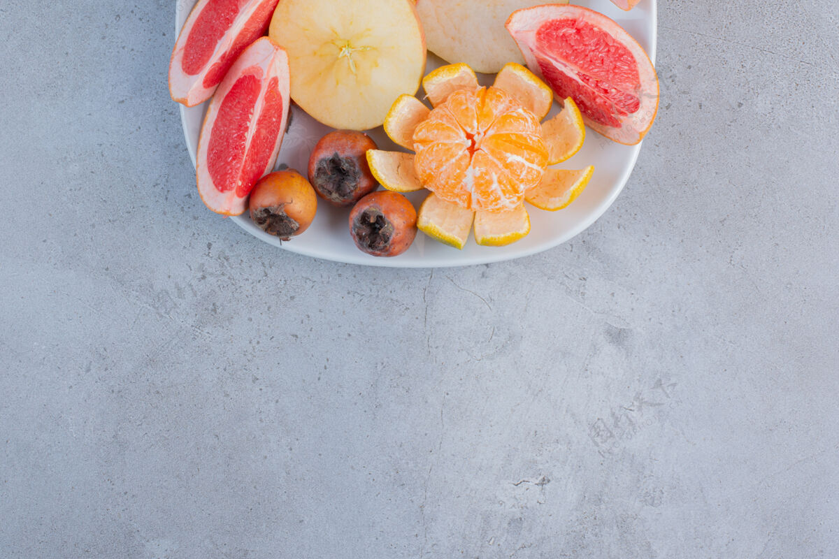 美味一盘切成片的葡萄柚 梨和一个削皮的橘子放在大理石背景上果皮风味天然
