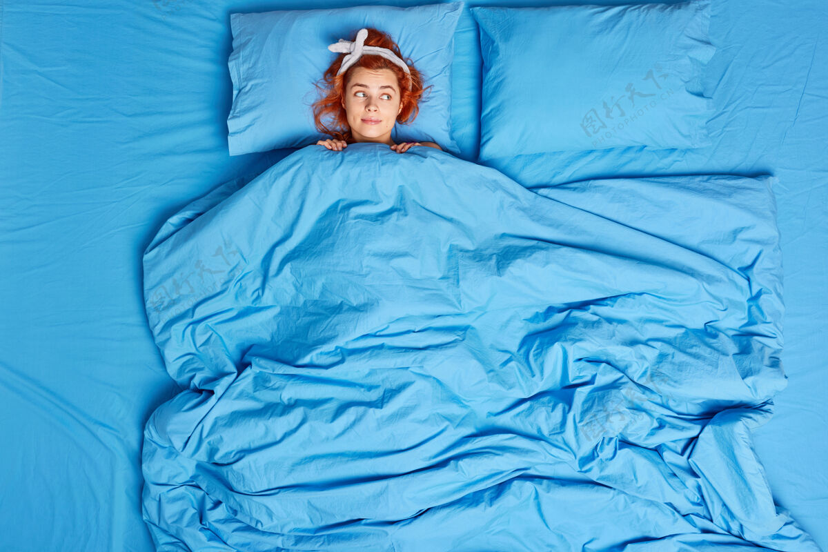 卧室红头发的欧洲年轻女子躺在柔软的毯子下戴着头巾睡在舒适的卧室里享受早晨感觉舒服戴着头巾看着若有所思的计划一天早晨睡衣人