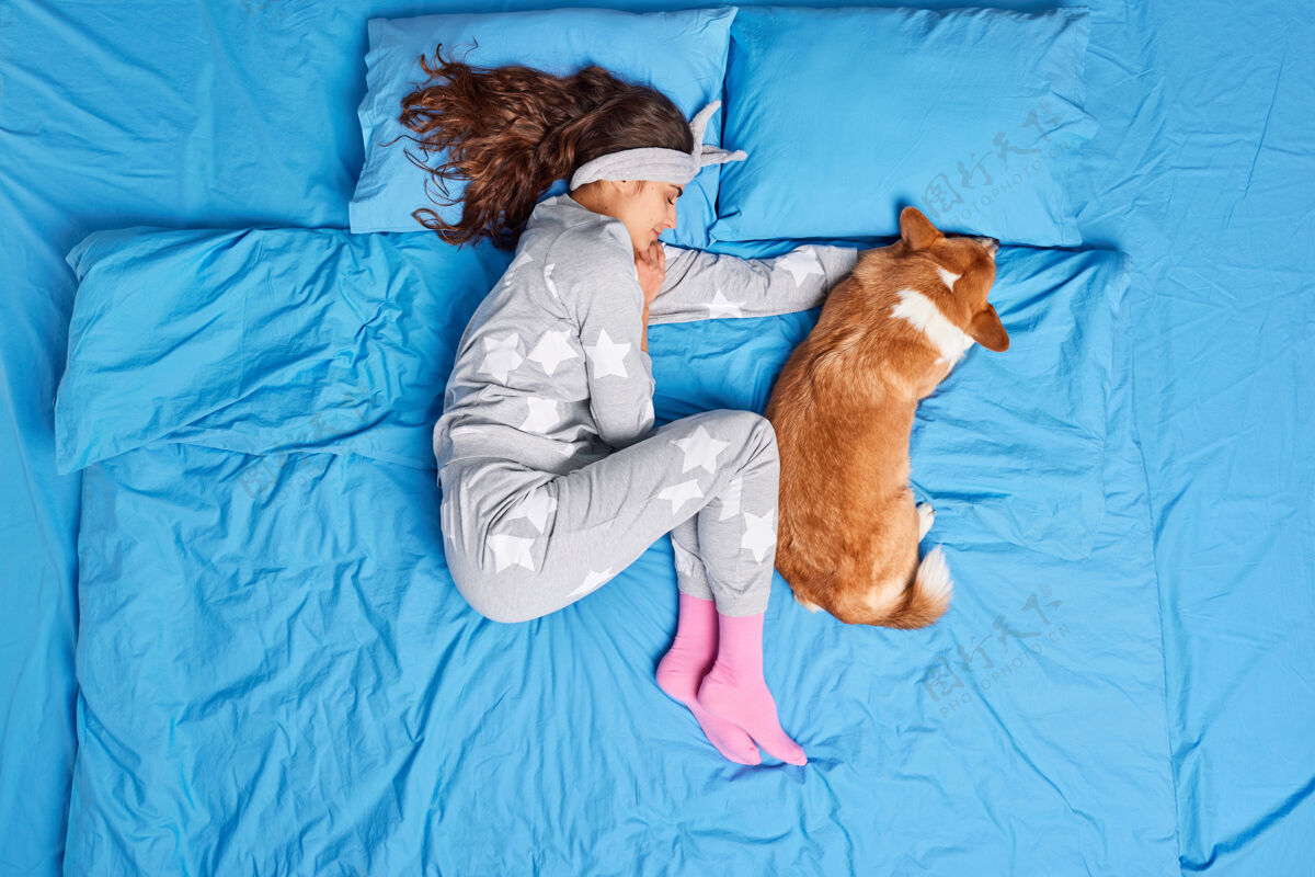 累了上图：深色皮肤的欧洲年轻女子穿着睡衣和心爱的宠物一起睡觉 看到甜美的梦 感觉舒服 在床上摆出健康的睡姿人们放松动物的睡前概念放松卧室枕头