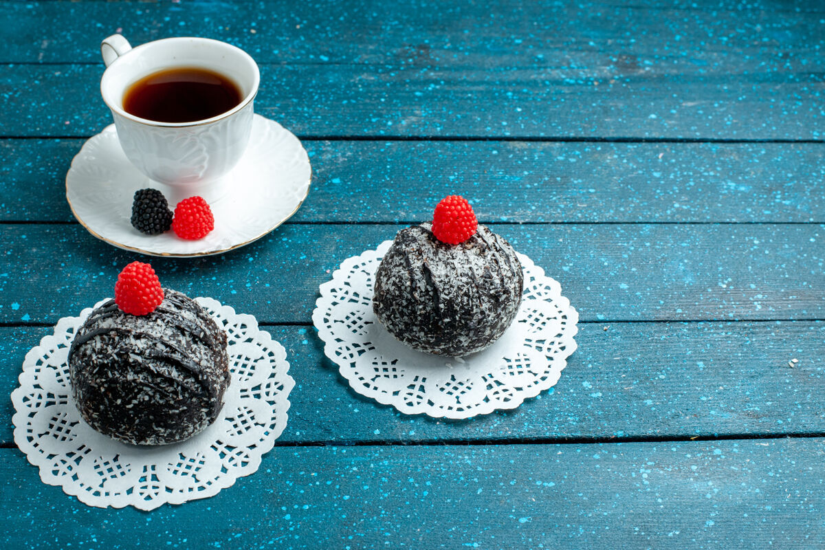 生的前视图美味的巧克力球与一杯茶在蓝色的乡村书桌上茶蛋糕饼干饼干甜容器乡村容器