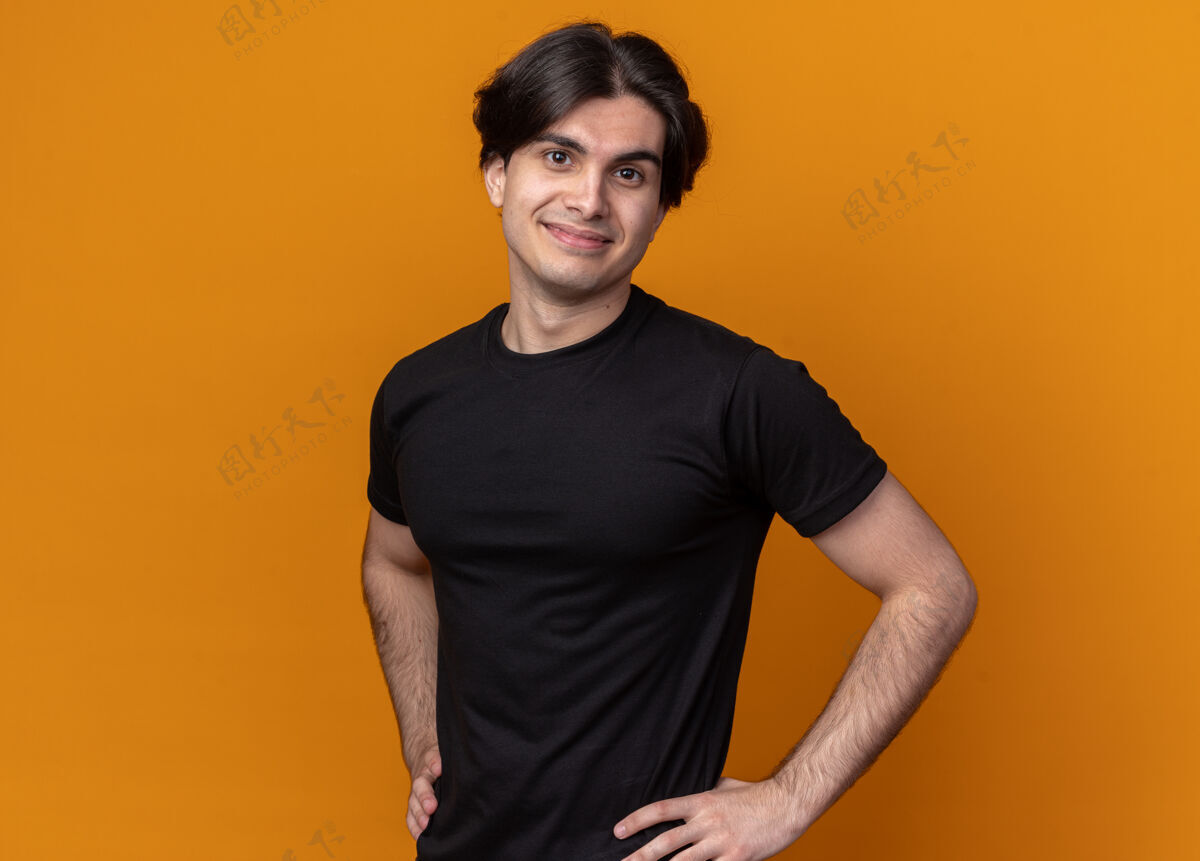 T恤高兴的年轻帅哥穿着黑色t恤把手放在臀部隔离在橙色的墙上手小伙子臀部