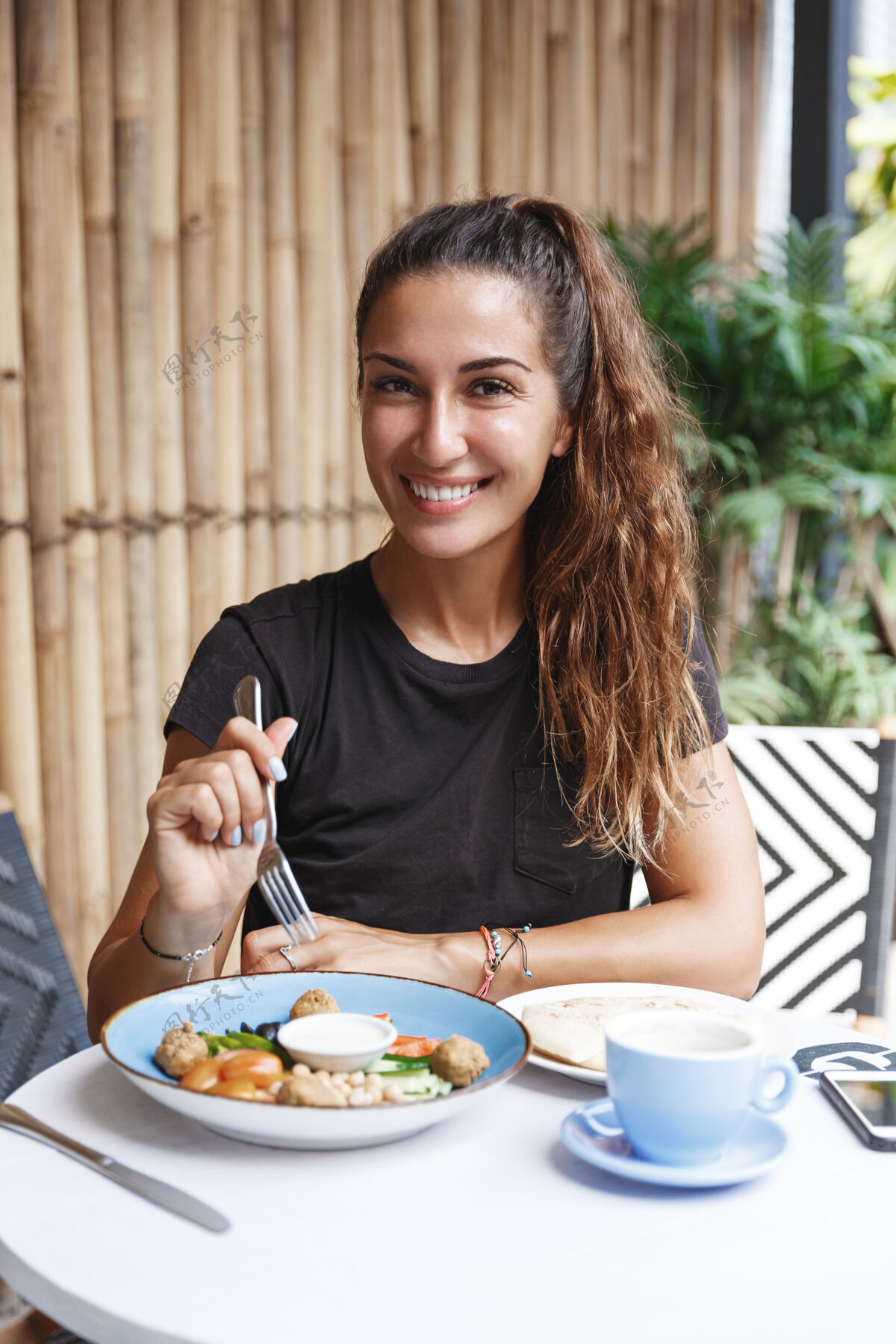年轻皮肤黝黑的健康女人 穿着t恤坐在咖啡厅露台上 吃着早餐 喝着咖啡休息咖啡午餐