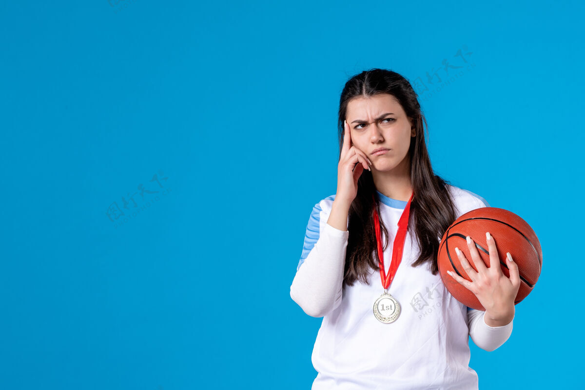 体育正面图：年轻女子拿着篮球站在蓝色的墙上手持人物人物