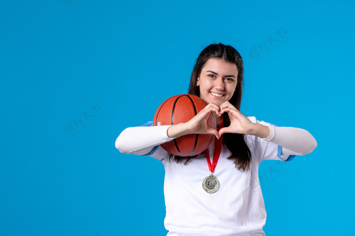 比赛正面图：年轻女子拿着篮球站在蓝色的墙上心年轻女性女人