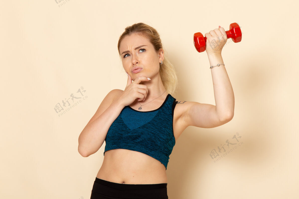 年轻女性正面图身着运动装的年轻女性手持红色哑铃 思考白墙运动健身美容操思考腹部视野