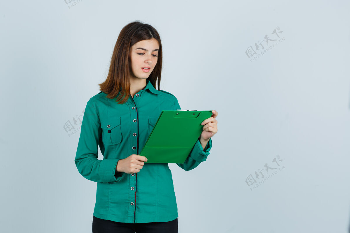沉思年轻女孩看着剪贴簿在绿色上衣 黑色裤子和期待集中 前视图女人人女士